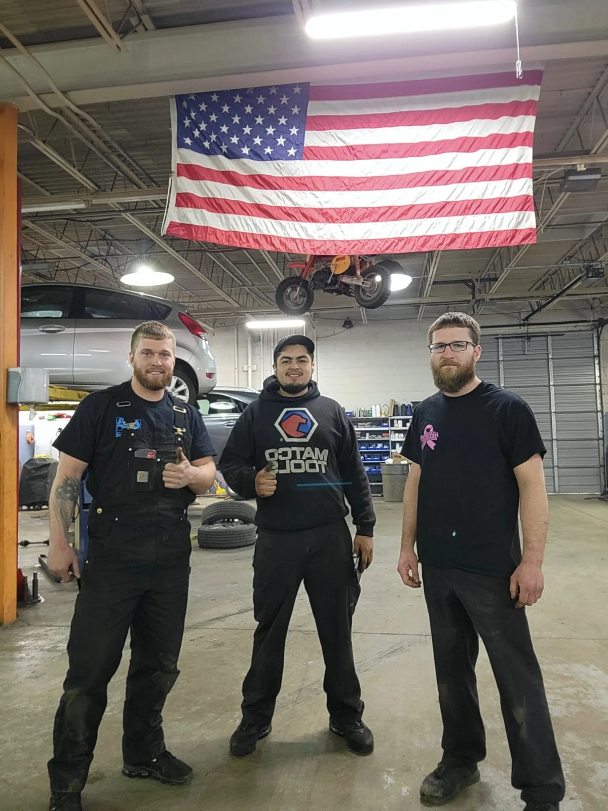Mint Hill Automotive team standing under American flag in shop